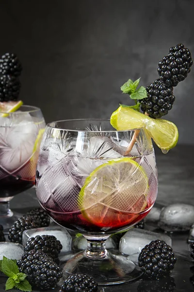 Seasonal soft drinks.Thirst in hot summer time. Two glasses of ice ,water ,lime and mulberry berries with mint on a dark background .Keto diet,soft drinks and alcoholic beverages. Fruit cocktail
