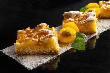 Koyu bir arka plan üzerinde sarı erik ve nane yaprakları ile süslenmiş pudra şekeri ile erik kek parçaları