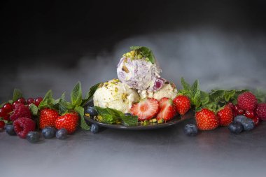 Taze çilek ile Vanilya ve dut dondurma topları, nane ve antep fıstığı serpilir. çilek, kuş üzümü, ahududu, koyu bir arka plan ve buhar ile yaban mersini . Yaz sezonu, sıcak yaz.
