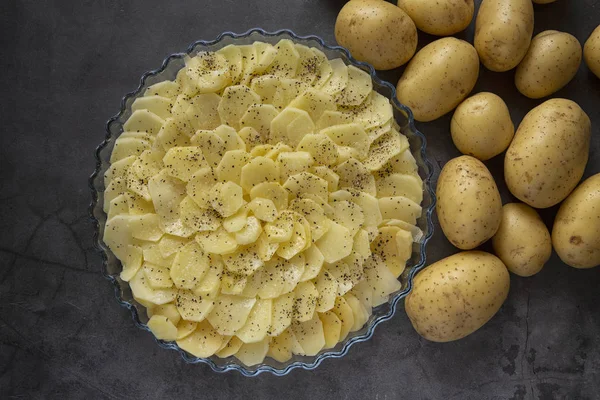 Cooking. Cooking baked potatoes in the oven.potato casserole, slices of fresh potatoes laid in a baking dish. Produce. Dark background