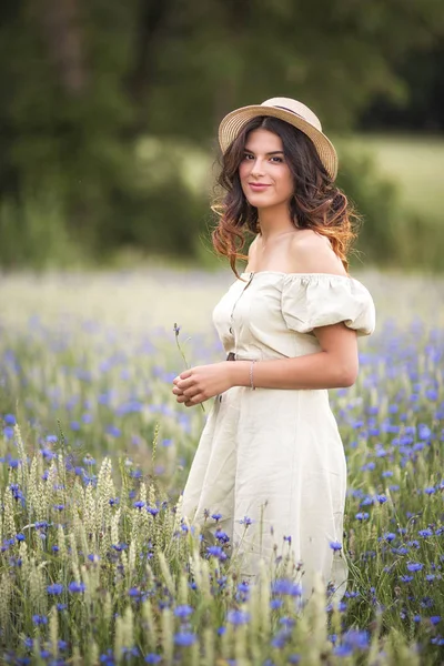 Ung vacker, mörkhårig flicka i en stråhatt i en blåklint fält i fältet. Sommar. spannmål och fält Dawns. Livet i byn. — Stockfoto