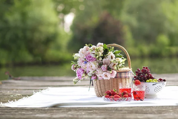 Picknick på sommaren. Korg med en bukett av pion blommor, frukt vin och jordgubbar och klasar av druvor Stockbild