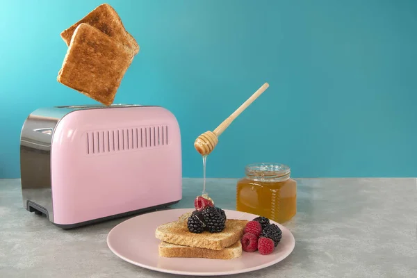 a pink toaster oven with leaping slices of fried bread on a blue background. Breakfast with honey and berries