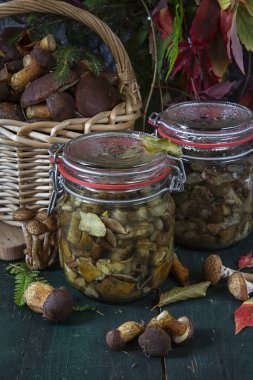 Mevsimlik mantar toplama. Kış için hazırlıklar, ev yapımı salamuralar. Ahşap bir masada mantarlı cam bir kavanozda marine edilmiş mantarlar. Sonbaharda orman.