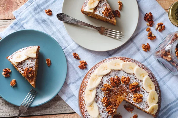 Pudra şekeri ve çatal ve cam tabakta ceviz ile dilimlenmiş muz pasta ile Flatlay deli dolu kavanoz. Ekose desenli Mutfak havlu ile ahşap arka plan üzerinde hafif tonlarda rahat üstten görünüm.