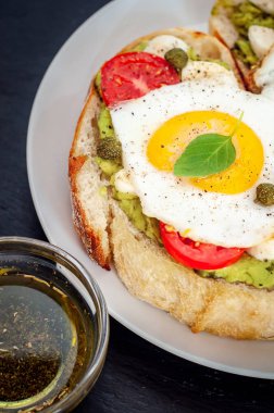 Agg, kiraz domates, mozzarella peyniri, avokado, fesleğen ve zeytinyağı sandviç tost. Karanlık bir taş zemin üzerine yan görünüm.