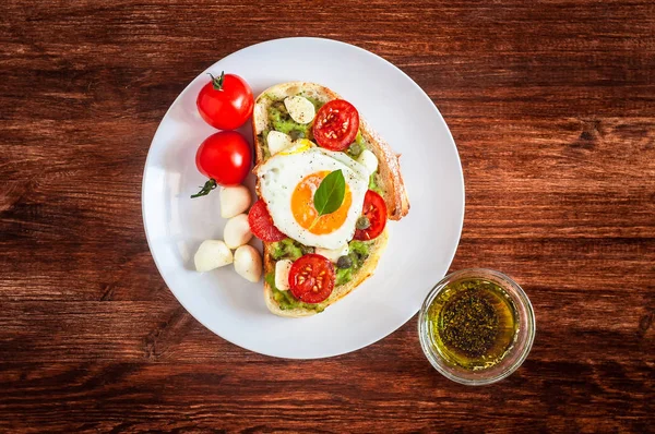 Agg, kiraz domates, mozzarella peyniri, avokado, fesleğen ve zeytinyağı sandviç tost. Üstten görünüm koyu ahşap arka plan üzerinde. Düz yatıyordu.