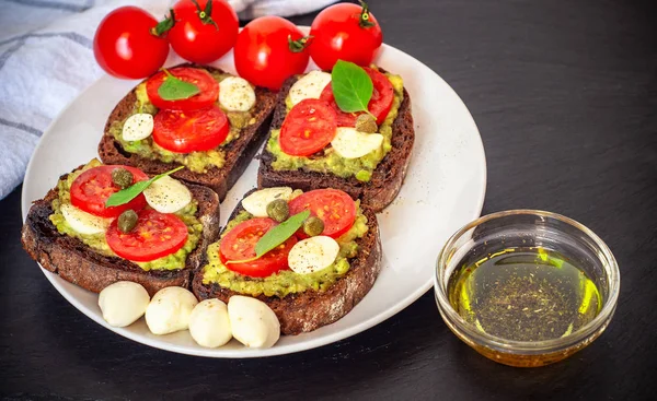 Kiraz domates, mozzarella peyniri, avokado, fesleğen ve zeytinyağı sandviç tost. Karanlık bir taş yemek yan görünüm.