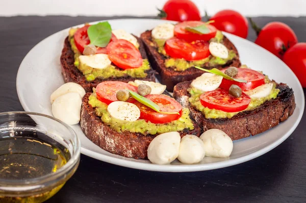 Kiraz domates, mozzarella peyniri, avokado, fesleğen ve zeytinyağı sandviç tost. Karanlık bir taş yemek yan görünüm.