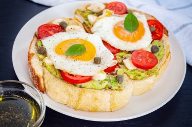 Agg, kiraz domates, mozzarella peyniri, avokado, fesleğen ve zeytinyağı sandviç tost. Karanlık bir taş zemin üzerine yan görünüm.