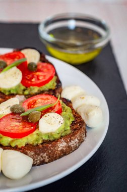 Kiraz domates, mozzarella peyniri, avokado, fesleğen ve zeytinyağı sandviç tost. Karanlık bir taş yemek yan görünüm.