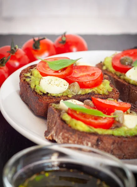 Kiraz domates, mozzarella peyniri, avokado, fesleğen ve zeytinyağı sandviç tost. Karanlık bir taş yemek yan görünüm.