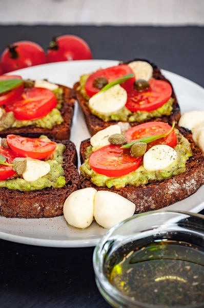 Kiraz domates, mozzarella peyniri, avokado, fesleğen ve zeytinyağı sandviç tost. Karanlık bir taş yemek yan görünüm.