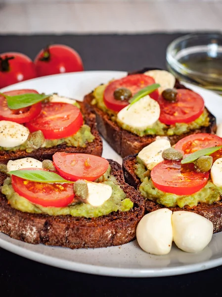 Kiraz domates, mozzarella peyniri, avokado, fesleğen ve zeytinyağı sandviç tost. Karanlık bir taş yemek yan görünüm