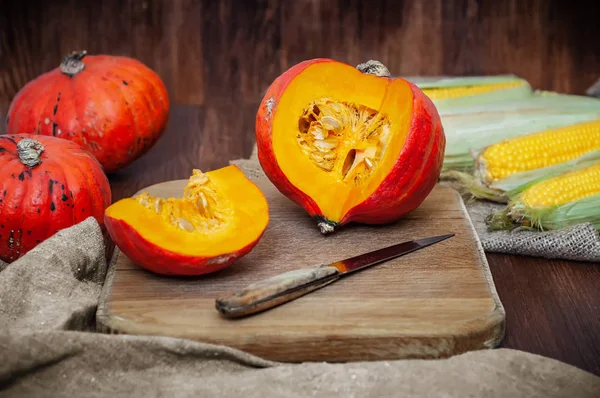 Dilimlenmiş ve bütün pumpkins, canvas kumaş ahşap zemin üzerine bıçakla kesme tahtası üzerinde Mısır. Yan görünümü natürmort rustik tarzda sonbaharda hasat ile.