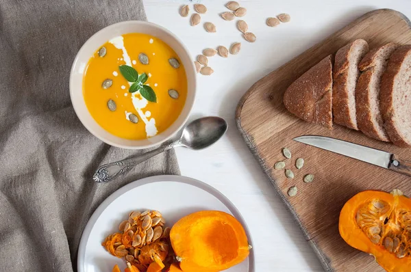 Kremalı kabak soupwith kabak tohumu ve yeşil, kepek ve ahşap üzerine dilimlenmiş kabak ekmek ve kumaş arka plan. Üstten görünüm