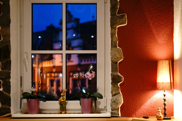 Идиллия интерьера у окна / Окно, украшенное цветами и растениями в интерьере жилого дома с прикроватной тумбой в вечернее время
.                        