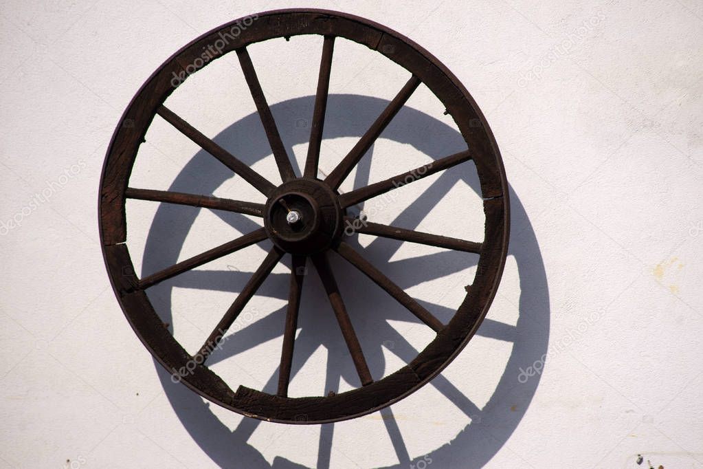 Decorative wooden spoke wheel / An old, nostalgic spoked wheel of a coach or a trailer hangs on the wall of a farmhouse for decorative purposes