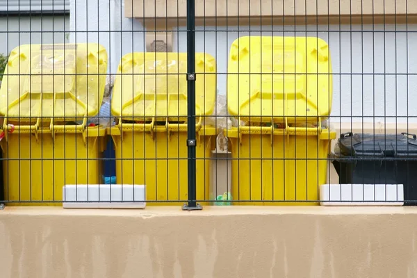 Yellow garbage cans / Yellow garbage cans stand in a row behind a mesh fence