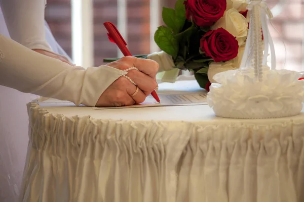 the bride signs on the marriage certificate, a bouquet of white and red roses on the table