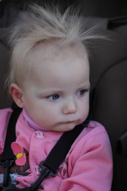 elektrikli saçlı pembe takım elbiseli küçük kız gülümsüyor ve yüzler yapıyor