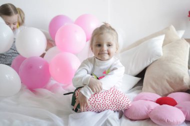 iki kız beyaz ve pembe balonlar ve çilek yastık ile yatakta oynamak