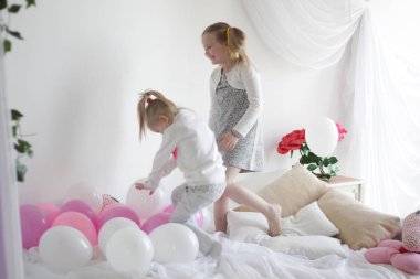 iki kız beyaz ve pembe balonlar ve çilek yastık ile yatakta oynamak