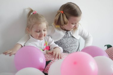 iki kız beyaz ve pembe balonlar ve çilek yastık ile yatakta oynamak