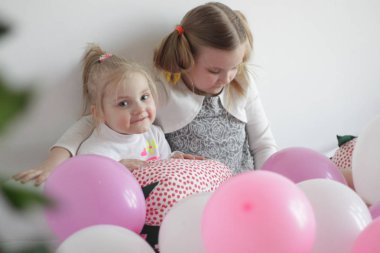 iki kız beyaz ve pembe balonlar ve çilek yastık ile yatakta oynamak
