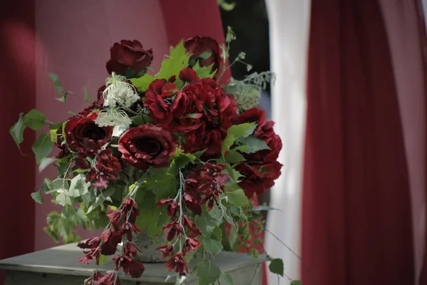 red flowers in a vase on a background of red and white fabric drapery