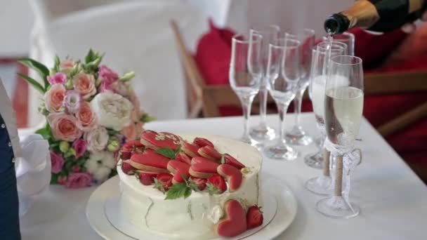 テーブルの上には イチゴとハートケーキ 花嫁のブーケ 装飾的な包装のシャンパンボトル ウェイターがグラスにシャンパンを注ぐケーキがあります — ストック動画