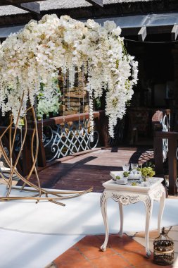Düğün dekoru: beyaz çiçek ve kristallerden oluşan büyük bir çelenk, çeşitli nesnelerle süslenmiş bir masa.