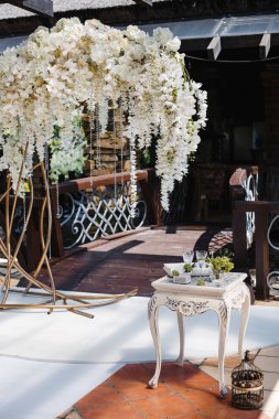 Düğün dekoru: beyaz çiçek ve kristallerden oluşan büyük bir çelenk, çeşitli nesnelerle süslenmiş bir masa.