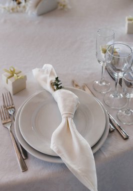 Masa ayarı: Tabaklar, çatallar, bıçaklar, düğümlenmiş peçete, gözlükler, küçük hediye kutusu