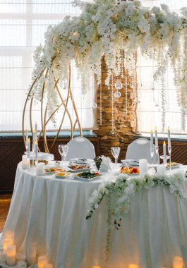 Yuvarlak bir ziyafet masası. Arkasında beyaz çiçekler olan kemer.