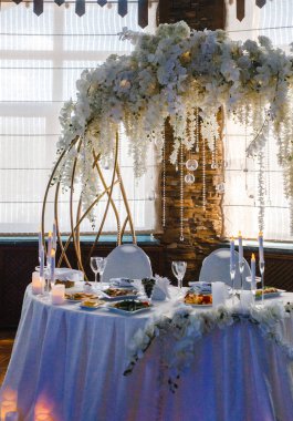 Yuvarlak bir ziyafet masası. Arkasında beyaz çiçekler olan kemer.