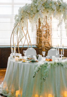 Yuvarlak bir ziyafet masası. Arkasında beyaz çiçekler olan kemer.