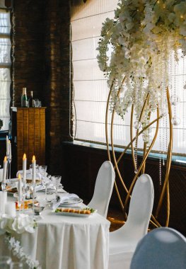 Düğün masasının arkasında beyaz çiçeklerle süslenmiş dekoratif kemer.