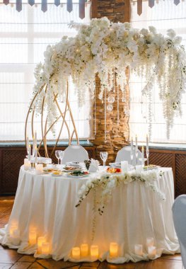 Yuvarlak bir ziyafet masası. Arkasında beyaz çiçekler olan kemer.