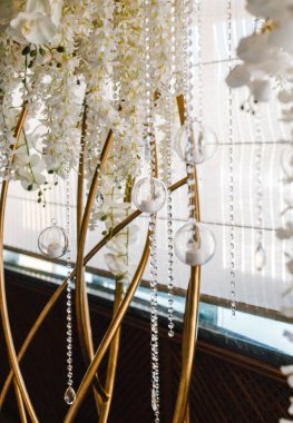 Düğün masasının arkasında beyaz çiçeklerle süslenmiş dekoratif kemer.