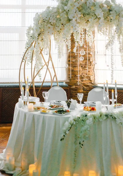 Yuvarlak bir ziyafet masası. Arkasında beyaz çiçekler olan kemer.