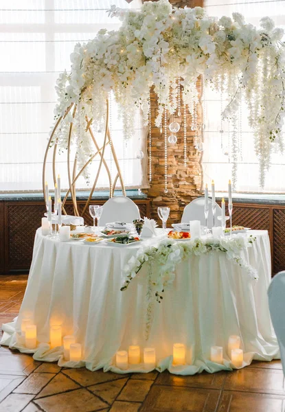 Yuvarlak bir ziyafet masası. Arkasında beyaz çiçekler olan kemer.