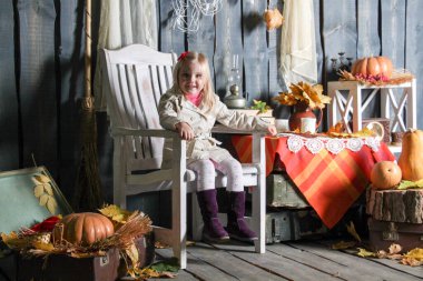 Cadılar Bayramı süslemelerinde bir sandalyede oturan, gülümseyen ve surat yapan bir kız.