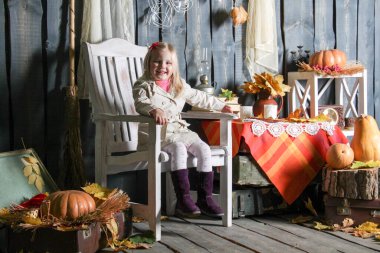 Cadılar Bayramı süslemelerinde bir sandalyede oturan, gülümseyen ve surat yapan bir kız.