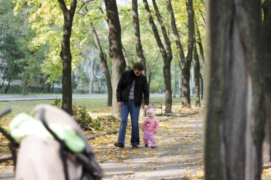 Baba ve kızı sonbahar parkında yürüyorlar.