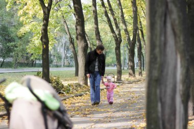 Baba ve kızı sonbahar parkında yürüyorlar.
