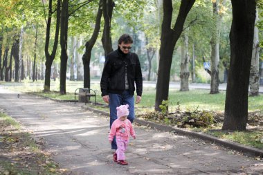 Baba ve kızı sonbahar parkında yürüyorlar.