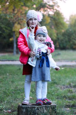 İki kız kardeş bir ağacın kütüğünde durur, sarılır ve gülümser.