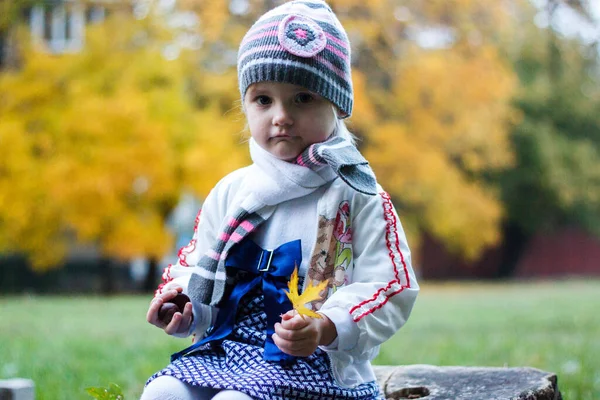 女の子は秋の公園の木の切り株に座って笑顔で顔を作っています — ストック写真