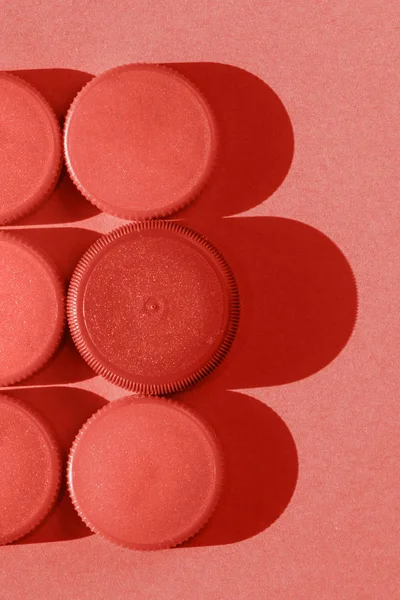 Coral color  plastic bottle caps on a coral background, the round caps are in two rows , monochromatic effect